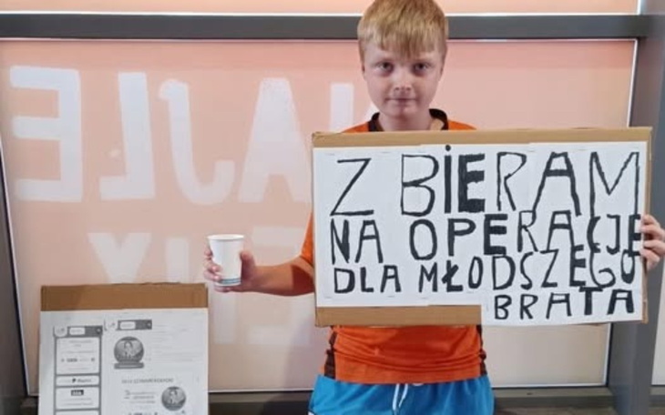 Chłopiec trzymający karton z napisem o zbiórce na operację.