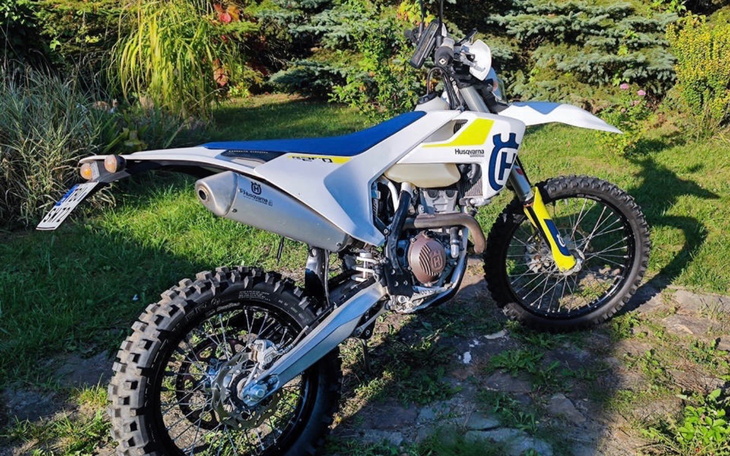 Motocykl terenowy na tle ogrodu, gotowy do jazdy.