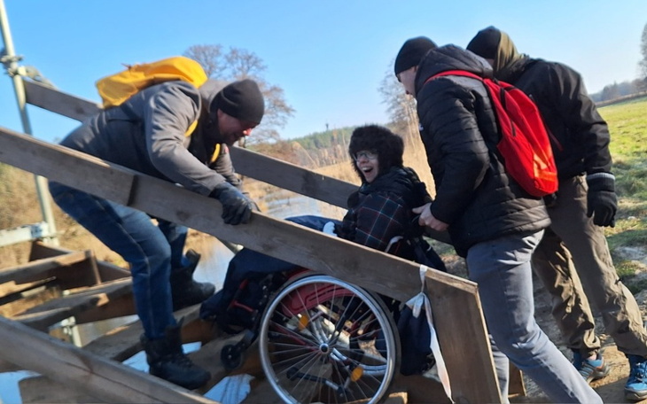 Grupa osób pomagająca w transporcie osoby na wózku.
