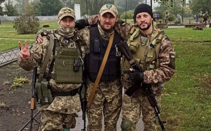 Trzej żołnierze w mundurach, pozujący do zdjęcia na tle zieleni.