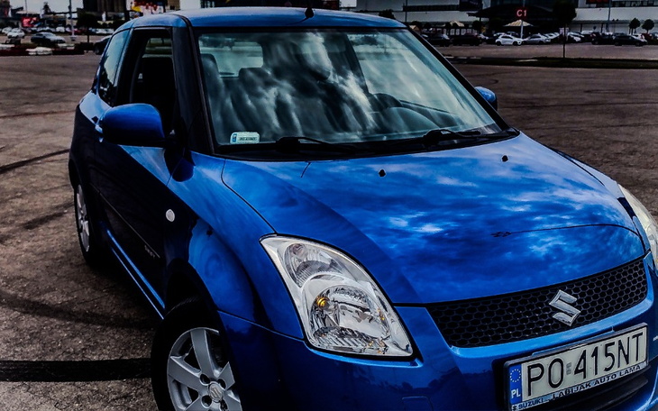 Niebieski samochód zaparkowany na parkingu z chmurami w tle.