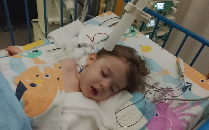Dziecko leżące w szpitalnym łóżku, z monitorami i rurkami medycznymi.