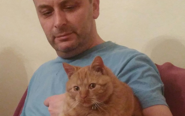 Mężczyzna trzyma kota na rękach, oboje wyglądają na zrelaksowanych.