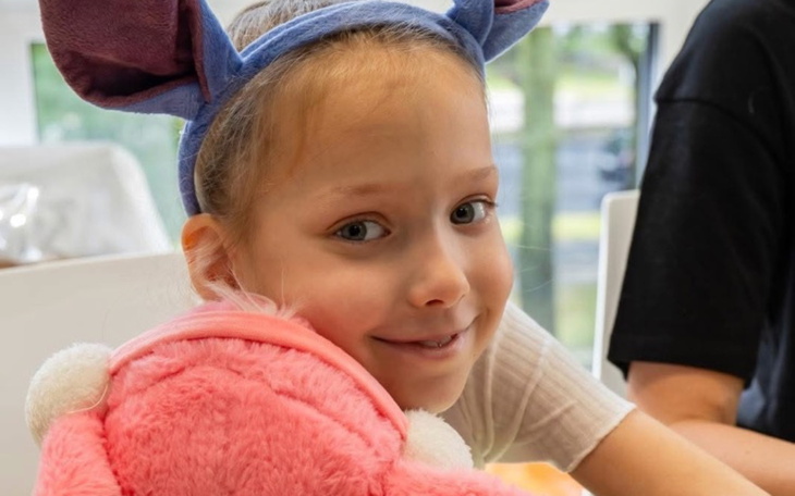 Uśmiechnięta dziewczynka z różowym pluszakiem i uszami.