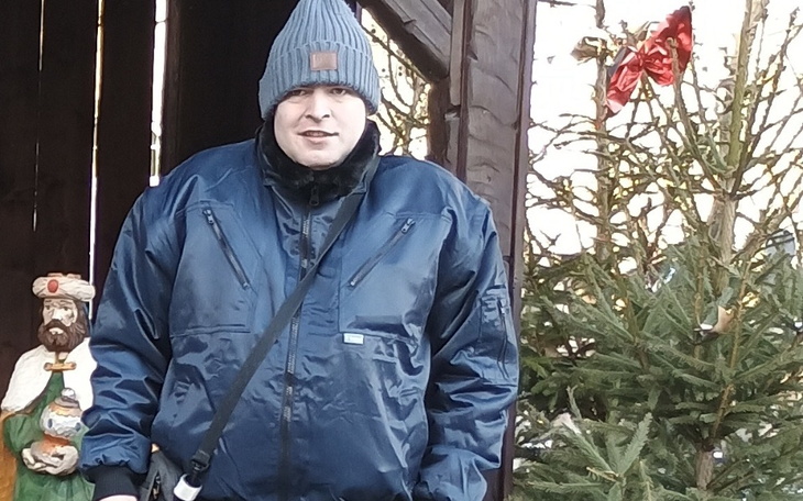 Mężczyzna w zimowej kurtce, pozujący na tle choinki.