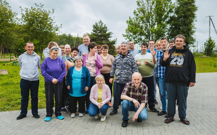 Grupa osób na świeżym powietrzu, uśmiechy i pozdrawianie do zdjęcia.