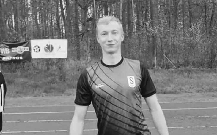 Młody mężczyzna w koszulce sportowej na boisku, uśmiechający się do kamery.