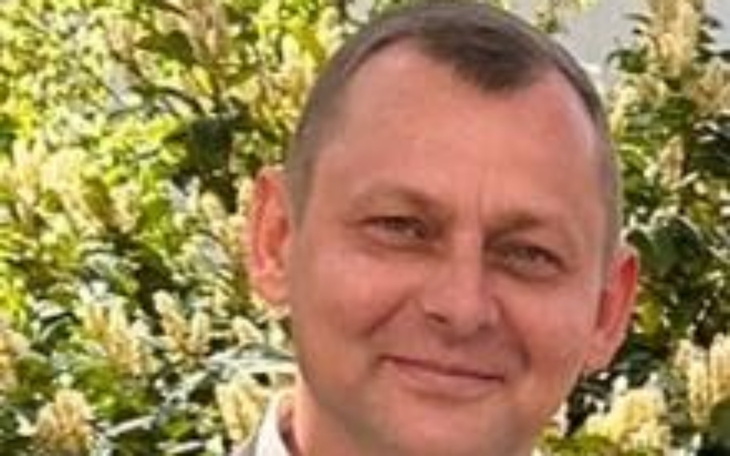 Mężczyzna uśmiechający się na tle zieleni.