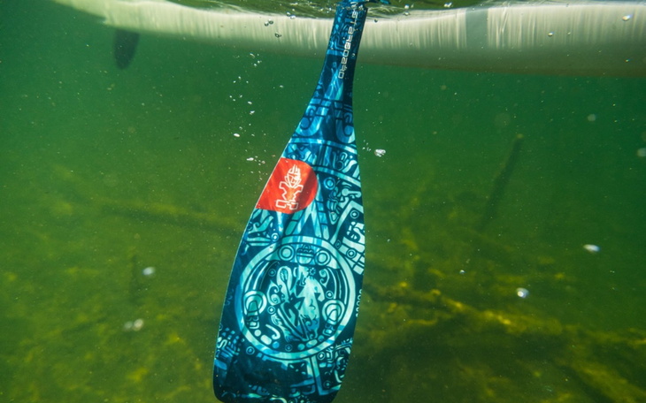 Wiosło zanurzone w wodzie, z kolorowym wzorem i logo.