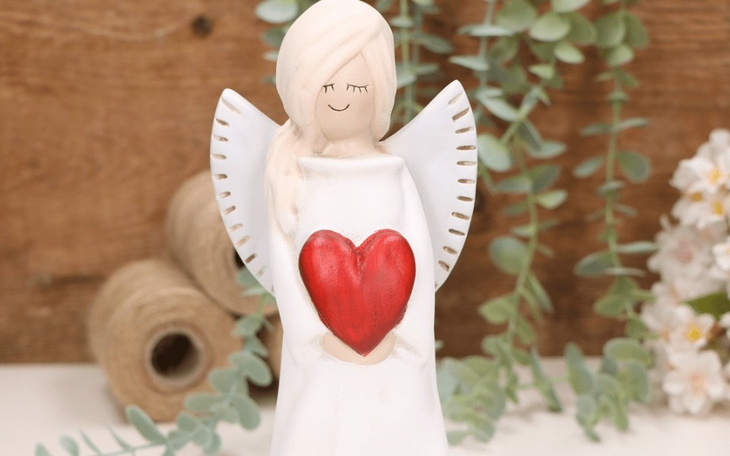 Figurka anioła trzymającego serce, otoczona roślinami.