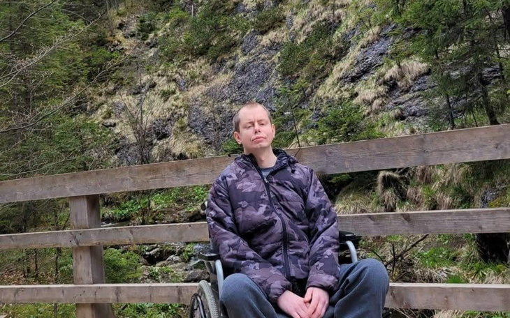 Mężczyzna na wózku inwalidzkim odpoczywa na drewnianym moście w otoczeniu natury.