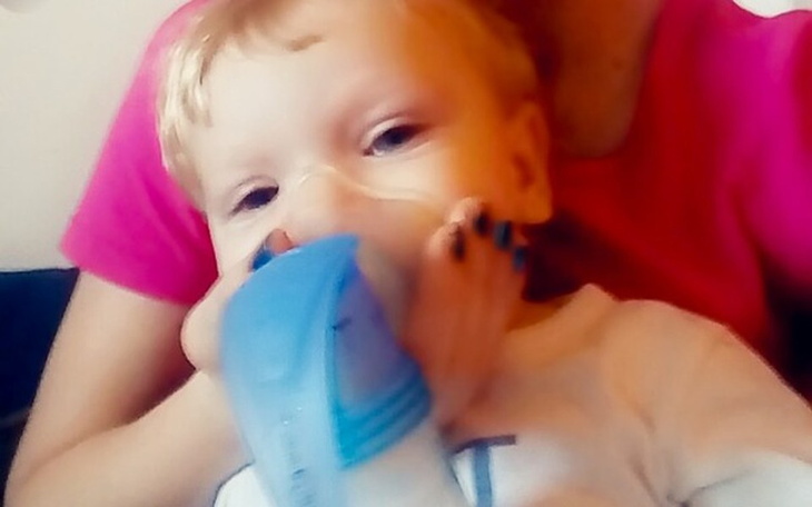 Chłopiec z maską tlenową, trzymany na rękach przez dorosłego.