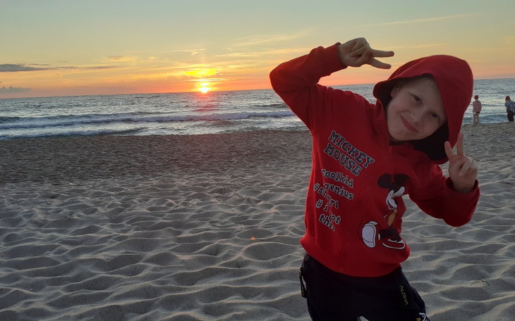 Chłopiec w czerwonym kapturze pozujący na plaży przy zachodzie słońca.