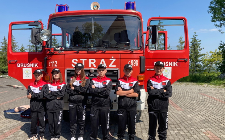 Grupa młodych strażaków przed wozem strażackim.