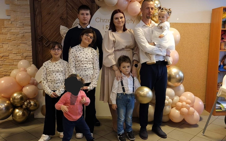 Rodzina pozująca na uroczystości z balonami w tle.