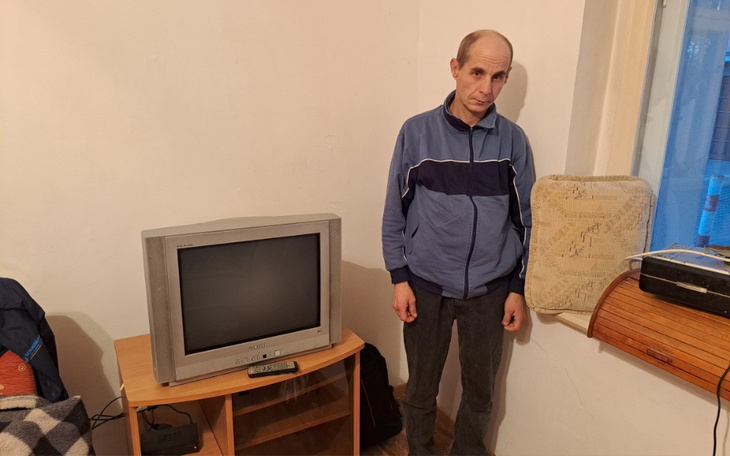 Mężczyzna w niebieskiej bluzie stoi obok starego telewizora.