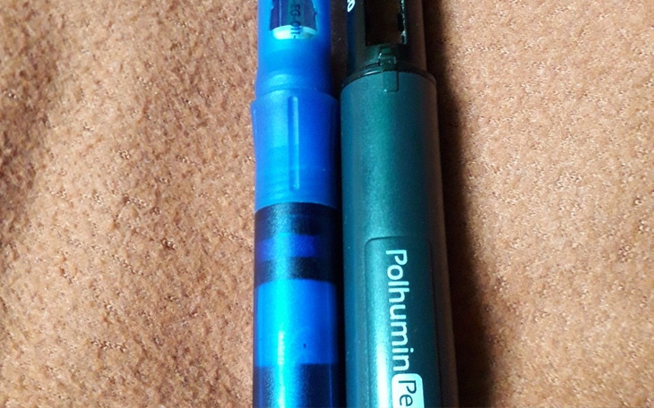 Dwa długopisy leżące obok siebie na brązowym tle.