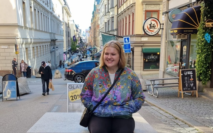 Młoda kobieta w kolorowej kurtce siedzi na ławce w mieście.