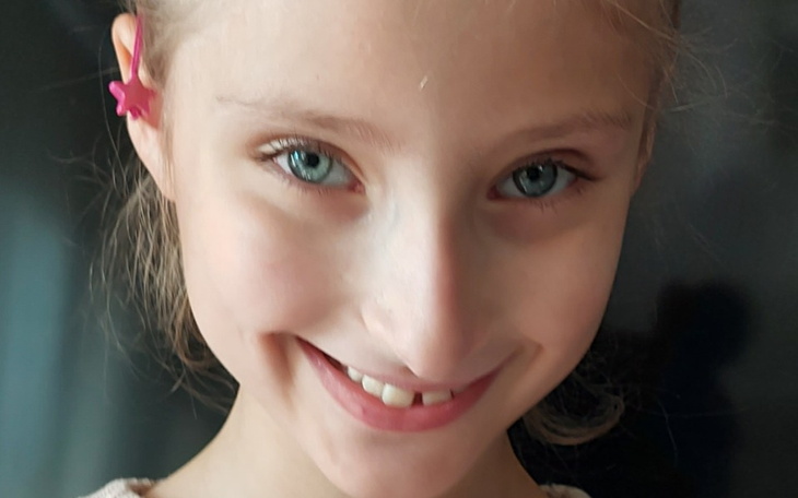 Uśmiechnięta dziewczynka z niebieskimi oczami i różowym klipsem.