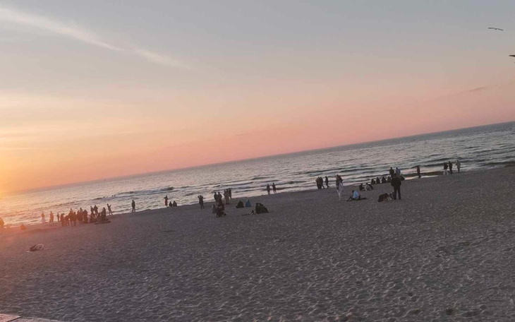 Plaża o zachodzie słońca, ludzie spacerujący po piasku.