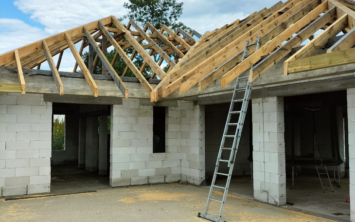 Budowa domu z drewnianym dachem, drabina oparta o ścianę.