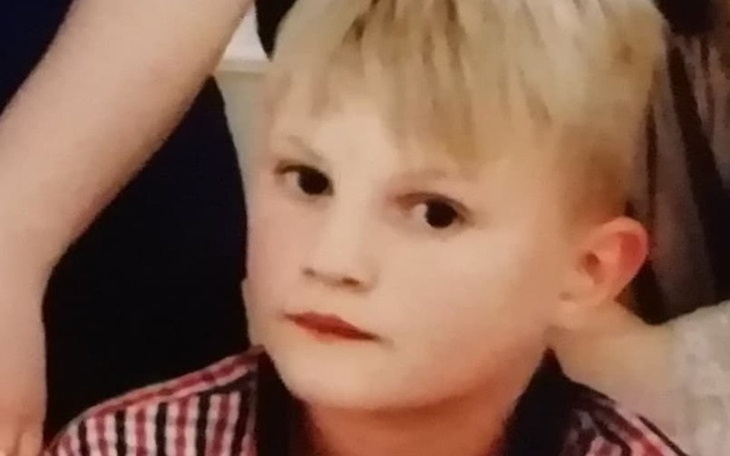 Chłopiec z blond włosami, patrzący w obiektyw z poważnym wyrazem.