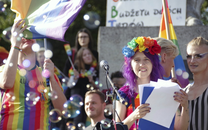 Ludzie na paradzie, trzymający tęczowe flagi i balony.