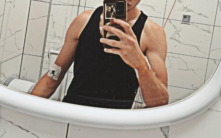 Młody mężczyzna w lustrze, pokazuje opatrunek na ramieniu.