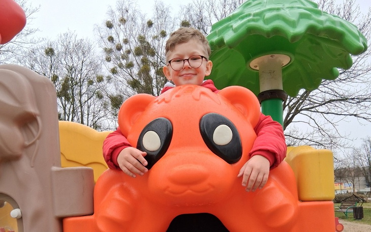 Chłopiec w okularach bawi się na placu zabaw, uśmiechając się.