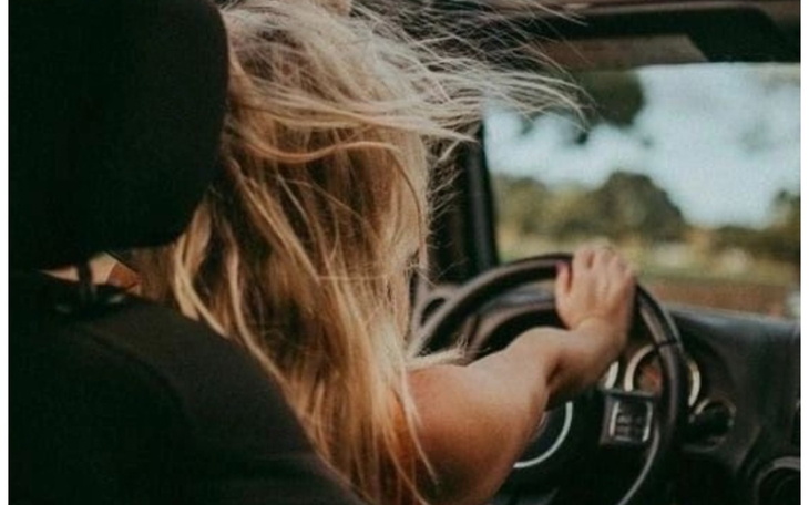 Kobieta prowadząca samochód z rozwianymi włosami.