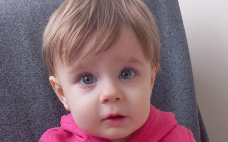 Mała dziewczynka z jasnymi oczami i blond włosami w różowym sweterku.