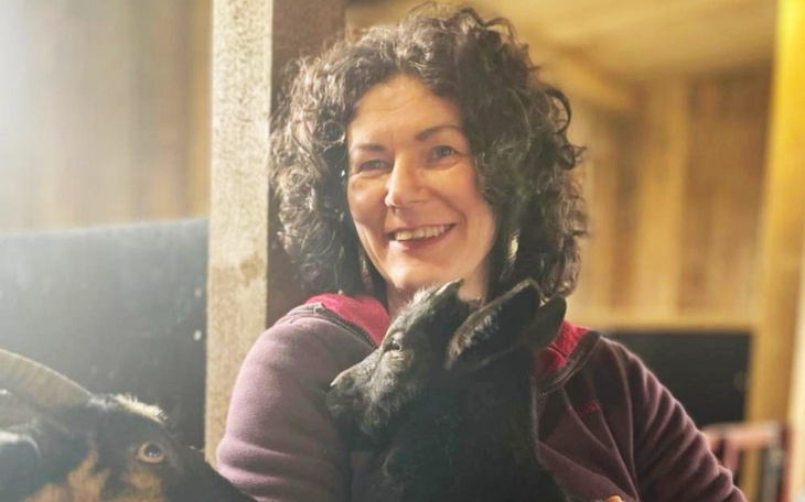 Uśmiechnięta kobieta trzymająca kozę na rękach.