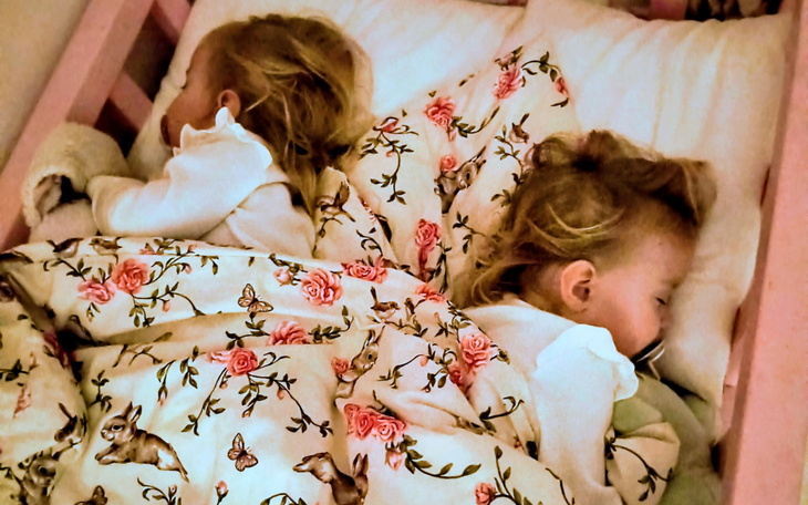 Dwie małe dziewczynki śpiące w łóżku pod kolorową pościelą.