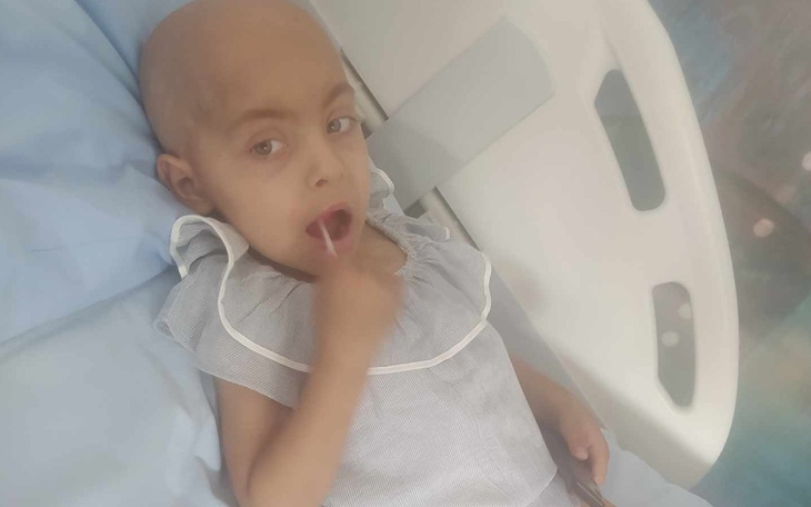 Dziecko w szpitalu, z uśmiechem, trzyma palec w buzi.