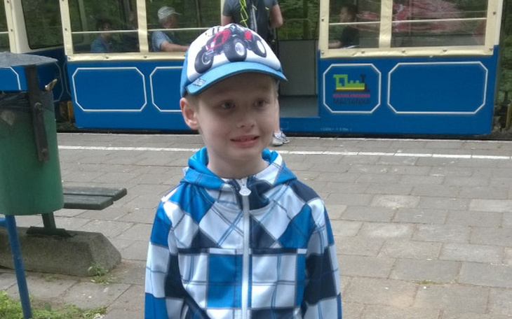 Chłopiec w czapce, uśmiechający się na tle tramwaju.