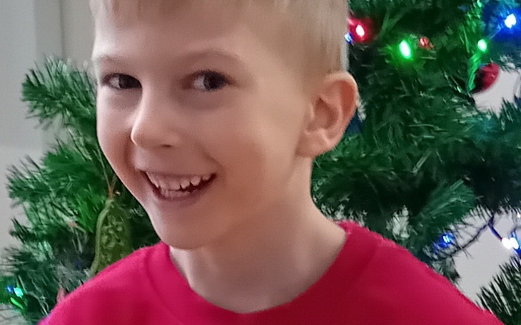 Uśmiechnięty chłopiec stojący przed choinką.