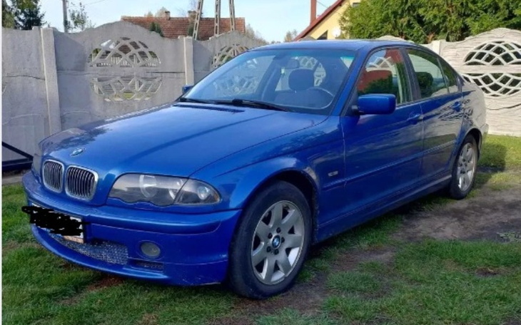 Niebieski samochód marki BMW zaparkowany na trawie.