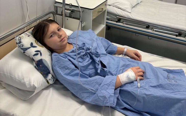 Dziewczynka w szpitalnym łóżku, w niebieskim szlafroku, z kroplówką.