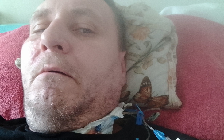 Mężczyzna leży na łóżku, z widocznymi rurkami medycznymi.