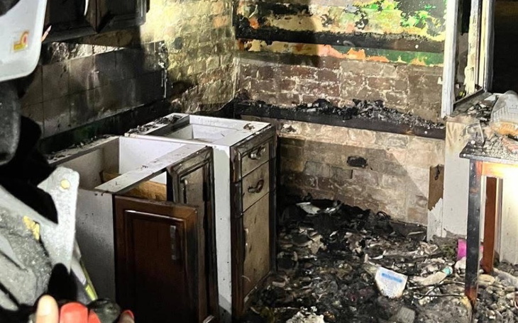 Zniszczona kuchnia po pożarze, z popiołem i zniszczonymi meblami.