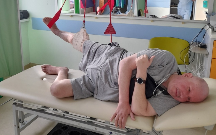 Mężczyzna w szpitalu, leżący na łóżku rehabilitacyjnym.