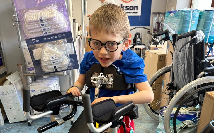 Chłopiec w specjalnym wózku, uśmiechający się do kamery.