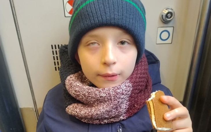 Chłopiec w czapce trzymający kanapkę, wygląda na zamyślonego.