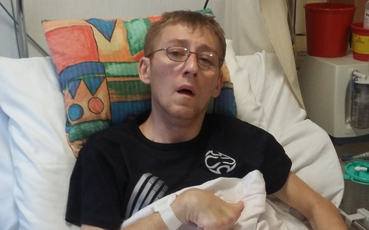 Mężczyzna w szpitalnym łóżku, wygląda na zmęczonego i osłabionego.