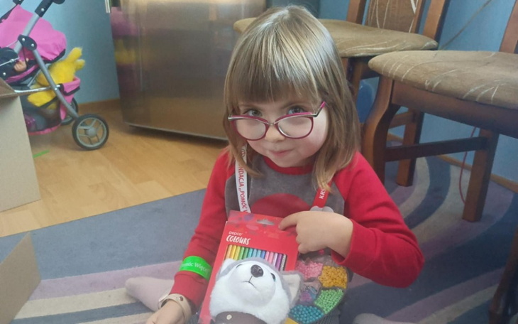 Mała dziewczynka z okularami, trzymająca kolorowe kredki.