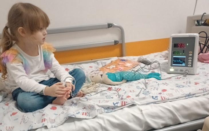 Dziewczynka w szpitalu z maskotką, monitor medyczny obok.