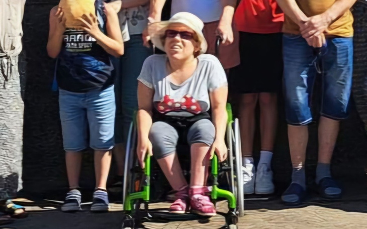 Grupa ludzi, w tym kobieta na wózku inwalidzkim, pozująca do zdjęcia.