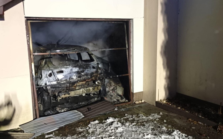 Spalony samochód w garażu, dym unosi się w powietrzu.