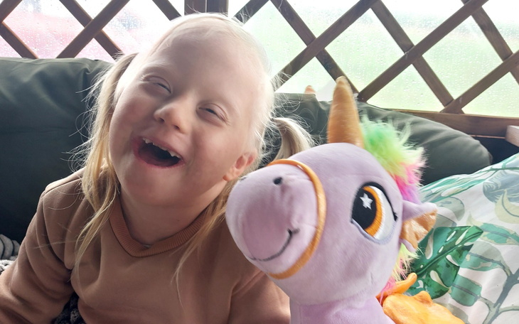 Dziewczynka z zespołem Downa, uśmiechająca się obok jednorożca.