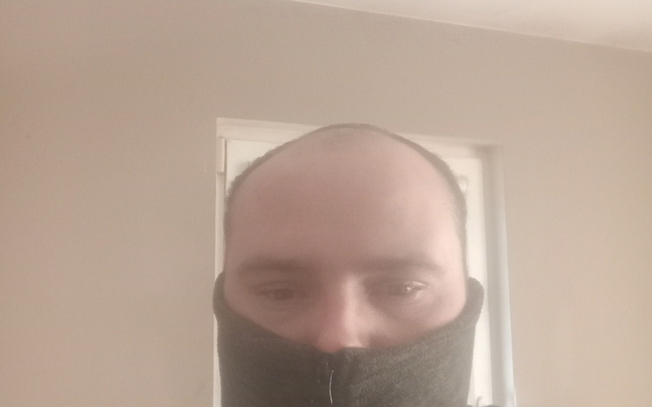 Mężczyzna w szarej czapce, z zamkniętą twarzą w szal.